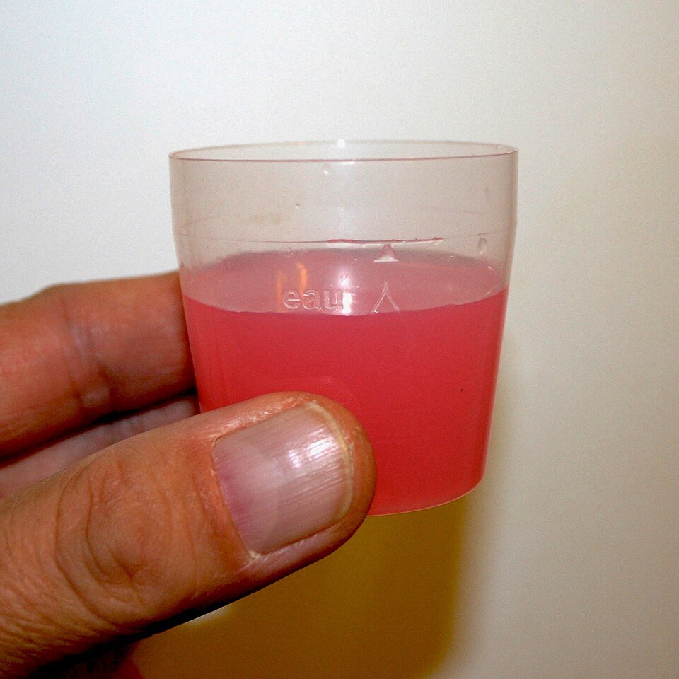 A glass of blue mouthwash next to its bottle, ready for rinsing